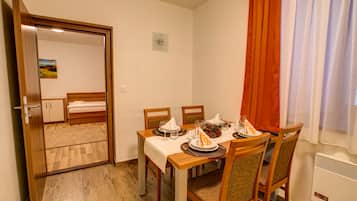 Una habitación compacta con una mesa de comedor dispuesta para cuatro personas, una cama y un pequeño ventanal con cortinas.