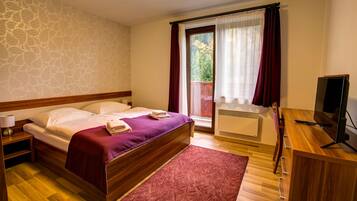 A bedroom with a bed, a desk, a chair, a TV, and a window with curtains.