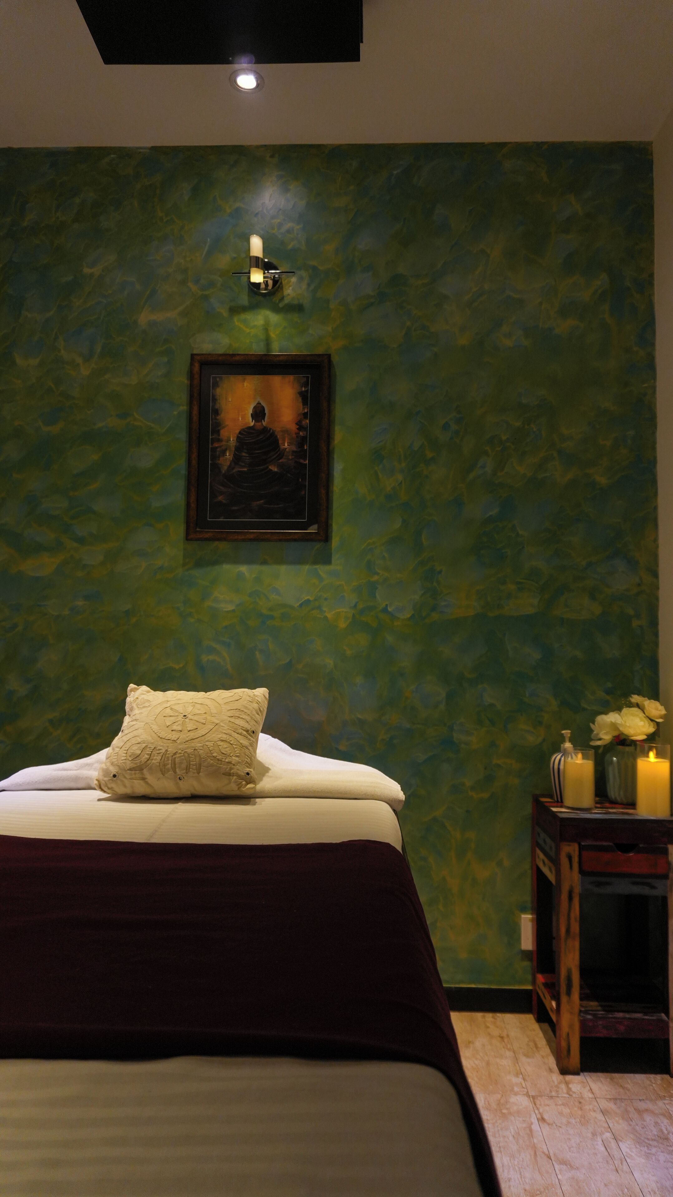 Une chambre avec un lit, un tableau encadré au mur, une table de chevet avec des bougies et un vase rempli de fleurs.