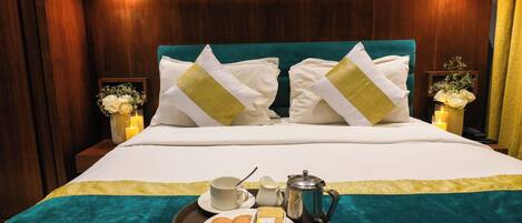 A neatly made bed with white and gold pillows, a teal bedspread, and a tray with breakfast items including cookies, butter, and a coffee pot.