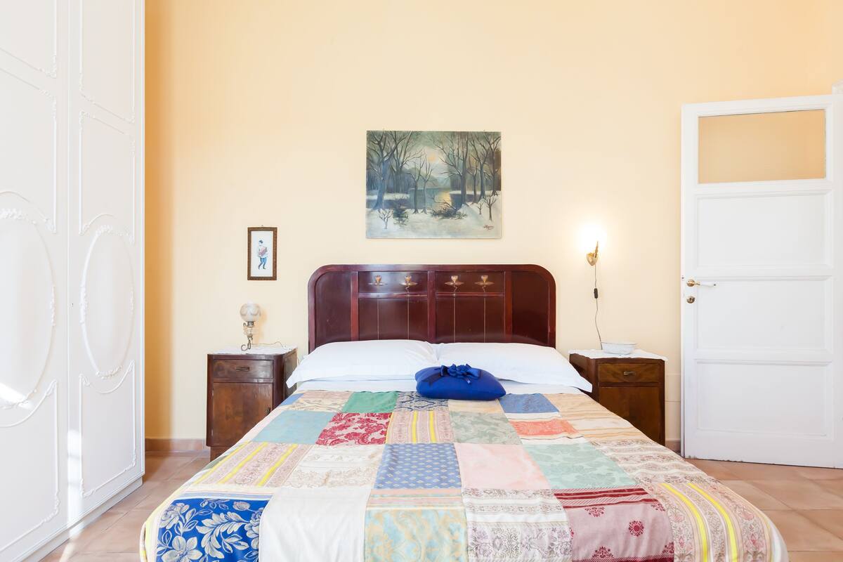 A bedroom with a wooden bed, a quilt, a painting on the wall, and a white door.