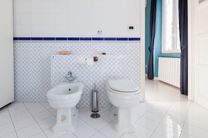 A bathroom with two white toilets, a bidet, a sink, and a blue and white tiled wall. - Terrace Suite (Rome)