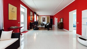 Ein großzügiger Wohnbereich mit rotem und weißem Farbkonzept, einem schwarzen Sofa, einem Couchtisch und einem schwarzen Sessel.