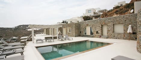 Zona de piscina en la azotea con sillones de descanso y un muro de piedra.