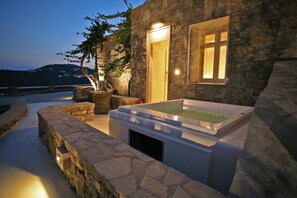 A stone building with a hot tub and a wooden door, surrounded by stone walls and a tree. - Atlantis Beach Residence (Mykonos)