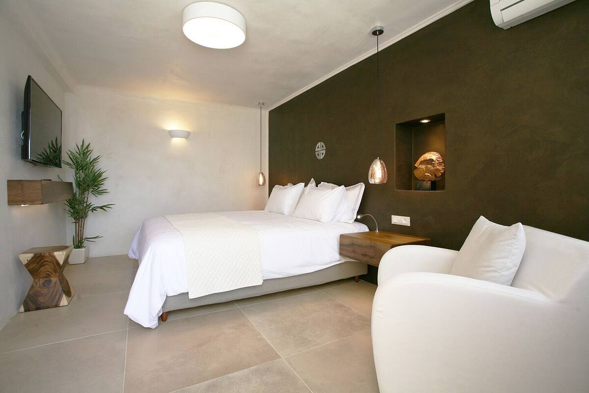 A modern bedroom with a bed, a sofa, a TV, and a wall-mounted shelf.