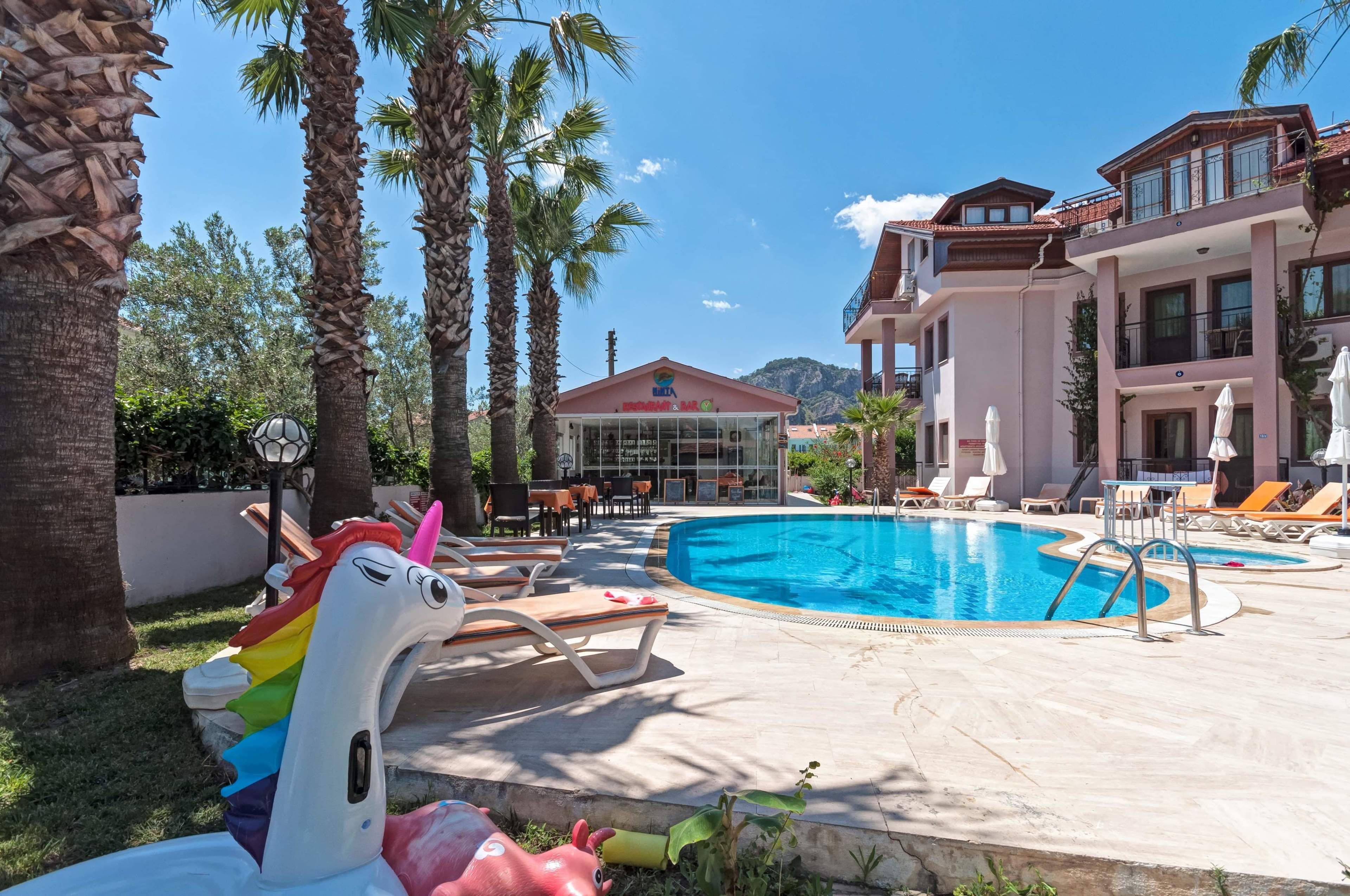 Un espace piscine avec des chaises longues, une décoration en forme de licorne et un bâtiment sur lequel on peut lire l’inscription « BETA ».