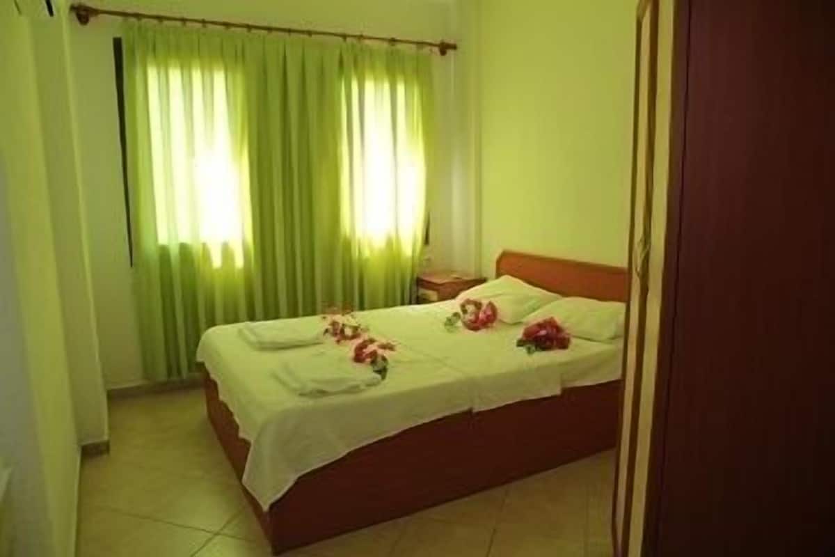 A bedroom with a bed, green curtains, and a nightstand.