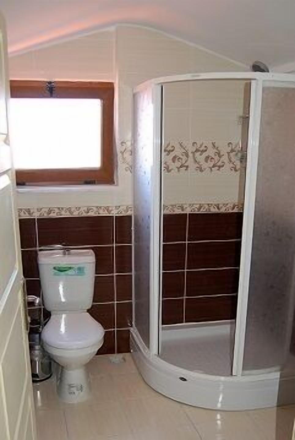 Un baño con inodoro, cabina de ducha y una ventana sobre el inodoro.