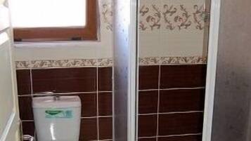 A bathroom with a toilet, a shower enclosure, and a window above the toilet.