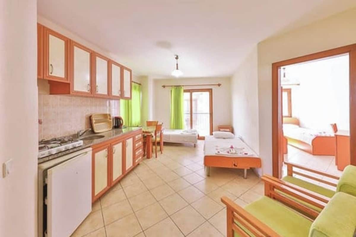 A compact room with a kitchenette, a bed, a small table, and a window.