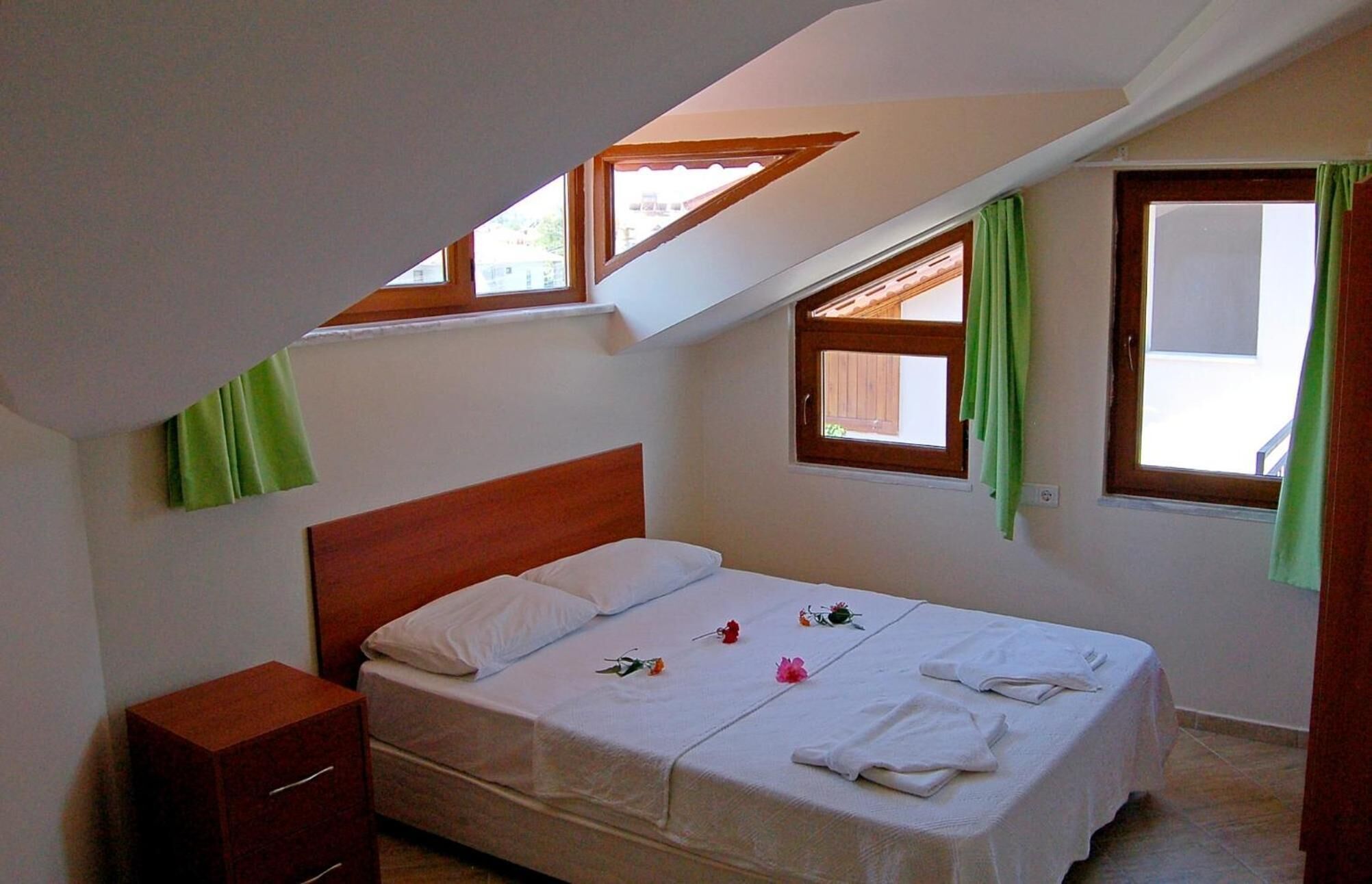 A bedroom with a single bed, a nightstand, and two windows with curtains.