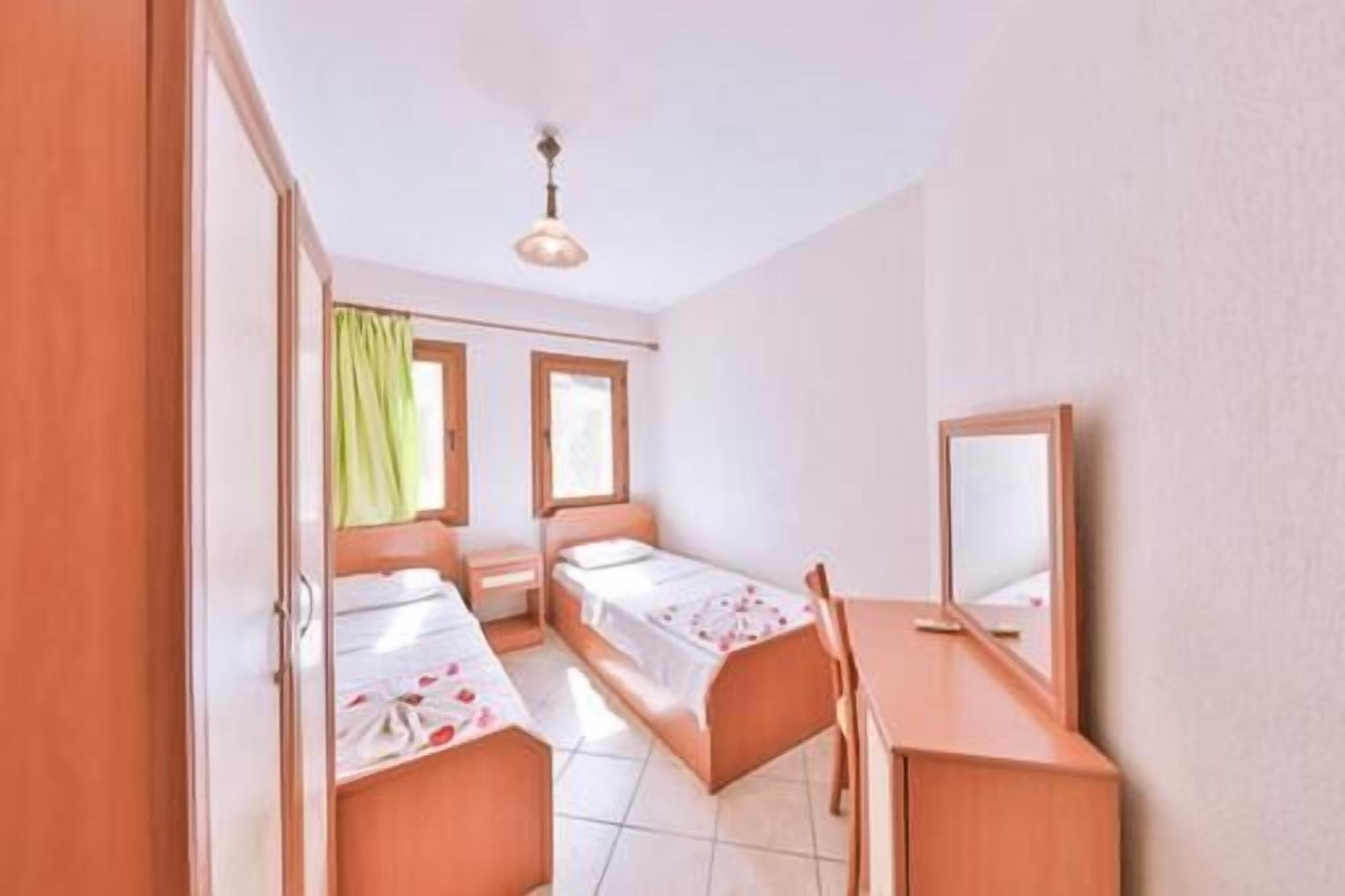 A bedroom with two single beds, a desk, a chair, a mirror, and a window with curtains.
