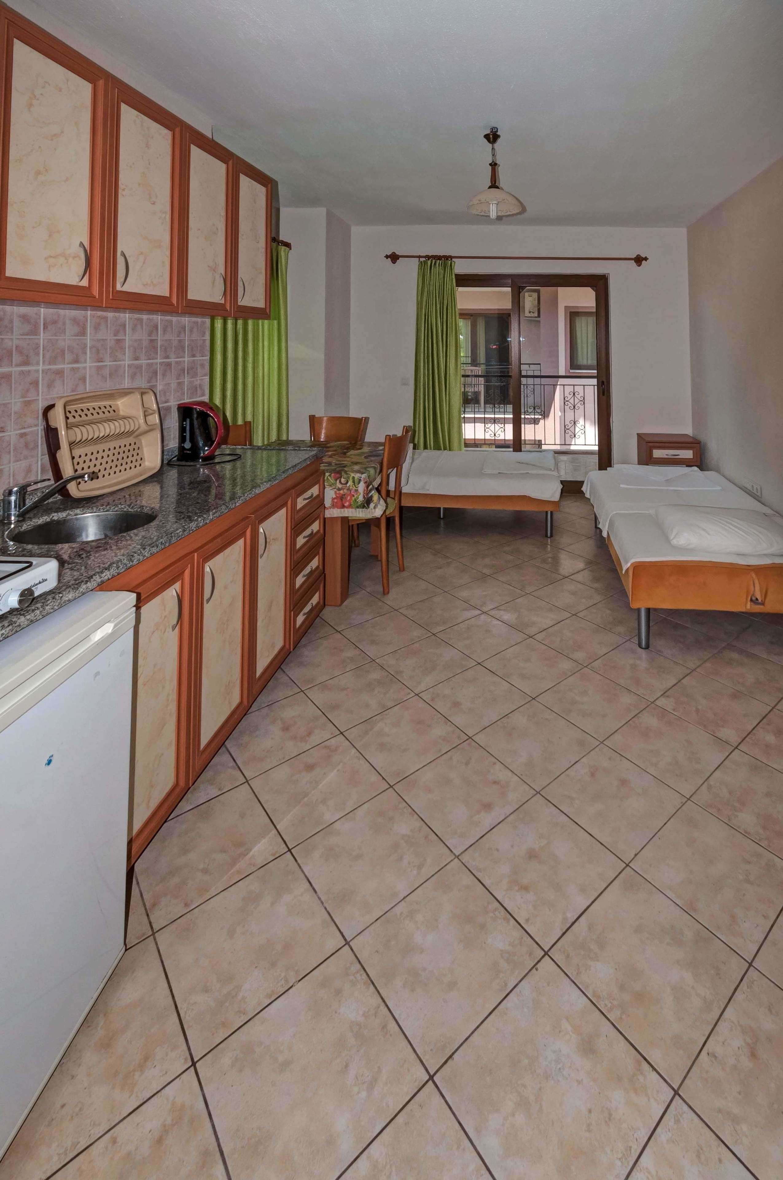 A compact hotel room with a kitchenette, two single beds, a dining area, and a view through a door.