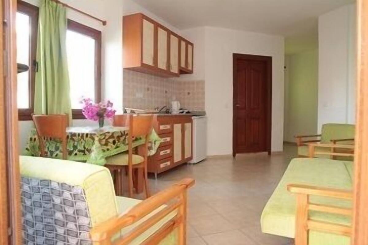 A compact kitchen with wooden cabinets, a dining table with chairs, and a small kitchenette area.