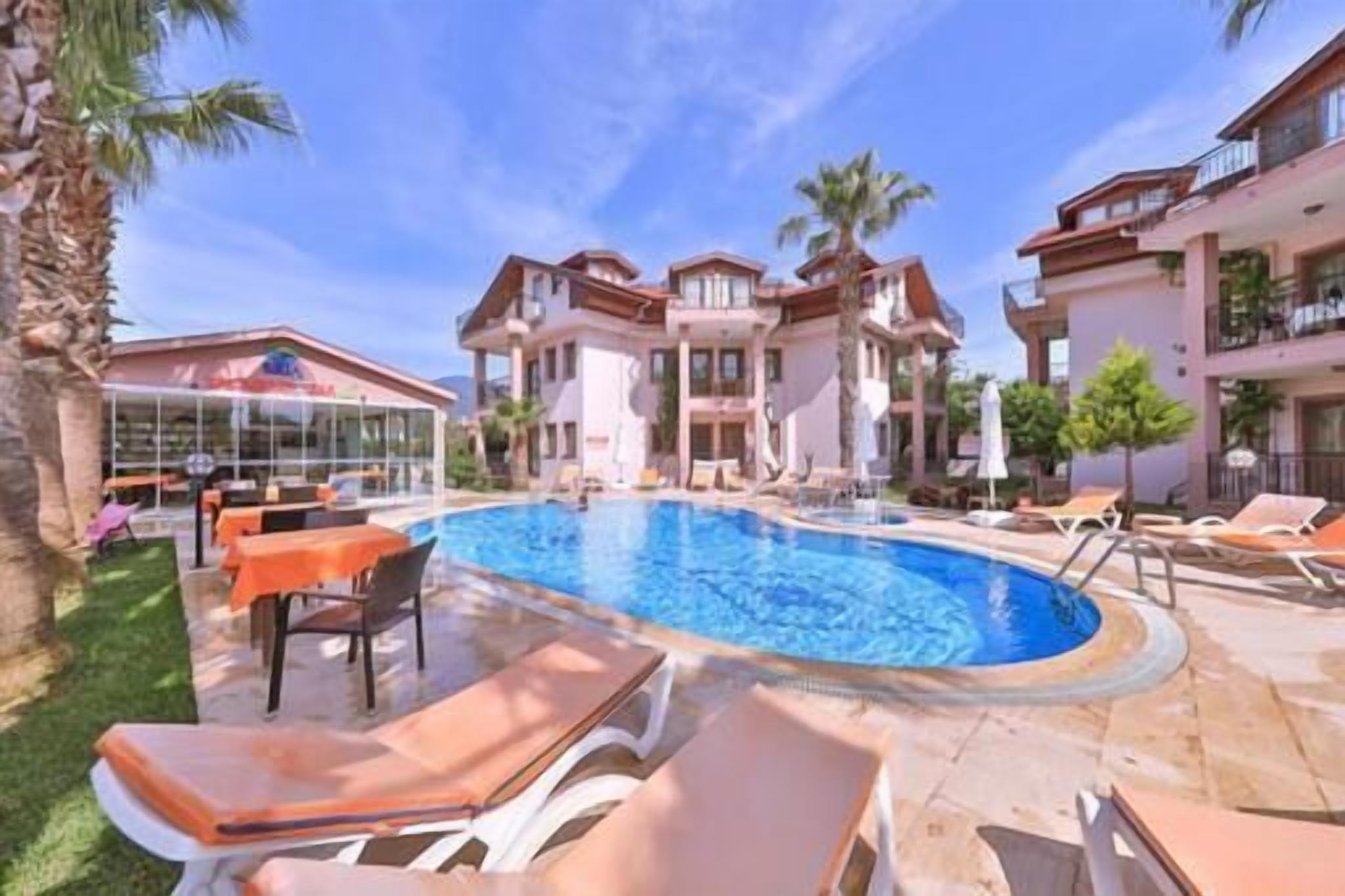 A hotel with a swimming pool, outdoor seating, and a building with balconies.