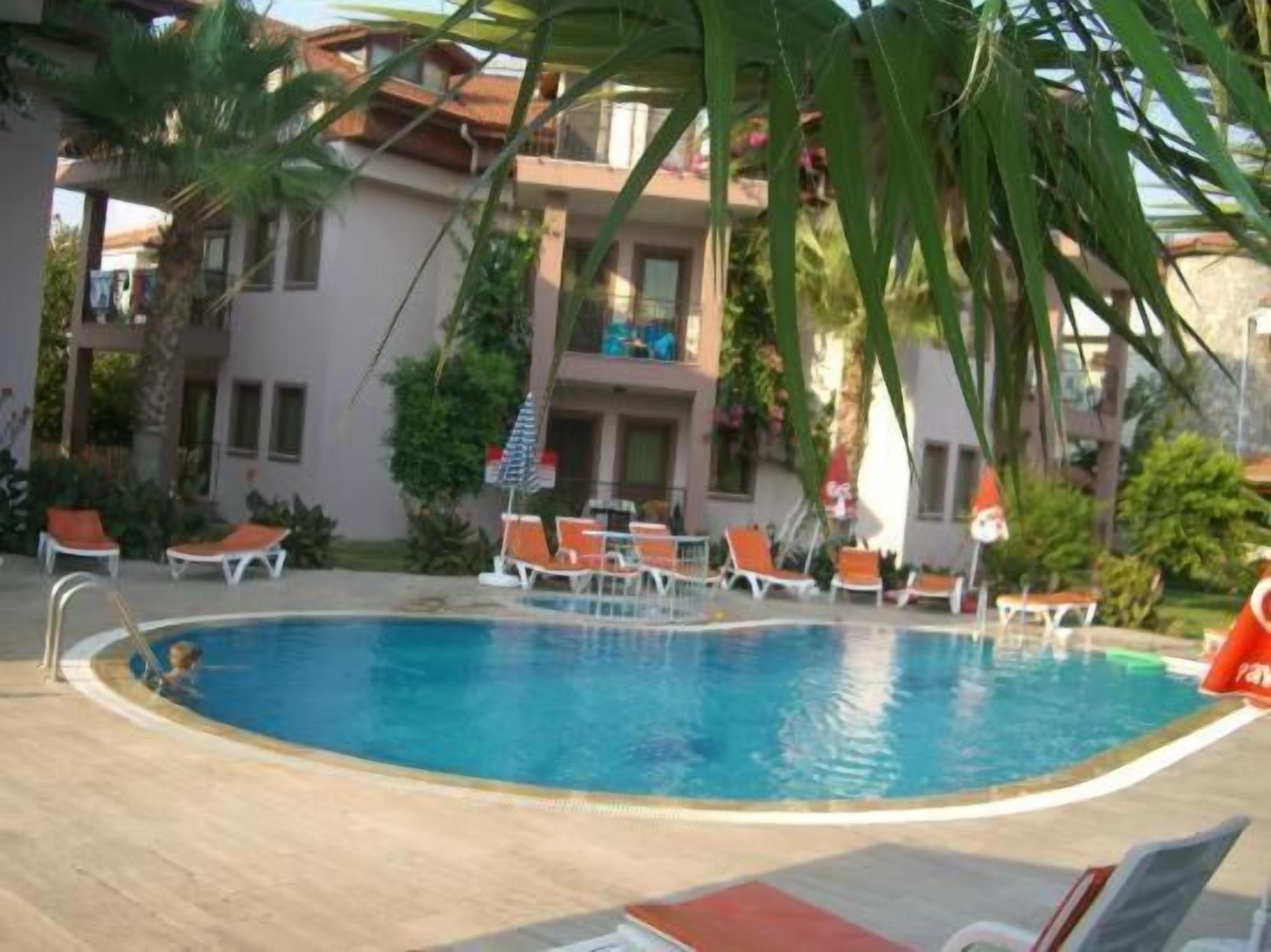 Zona de piscina con sillones de descanso y un edificio con balcones al fondo.