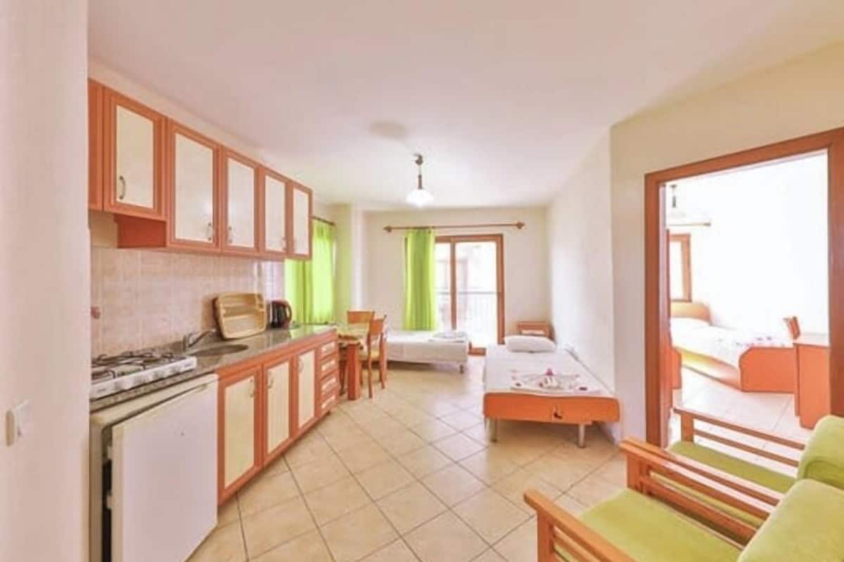 A compact room with a kitchenette, a bed, a small table, and a window.