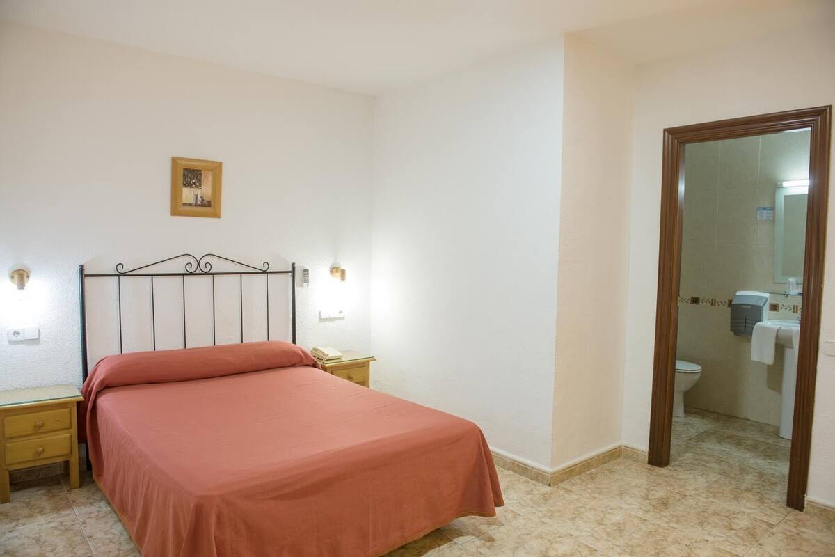 Une chambre à coucher avec un lit, une table de chevet, une lampe et un miroir qui reflète une salle de bain.