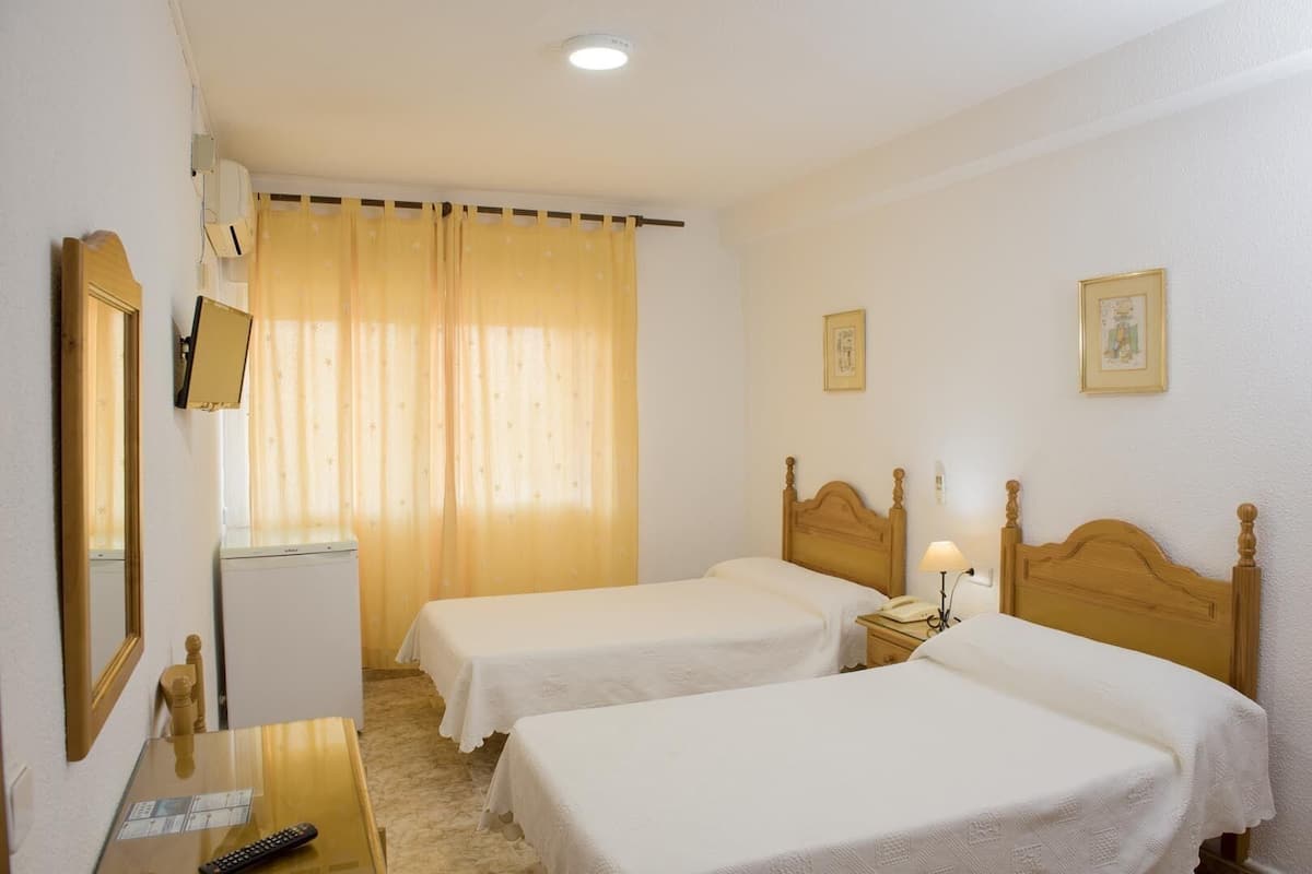 Une chambre d’hôtel avec deux lits simples, un bureau avec une chaise, un téléphone et un miroir.