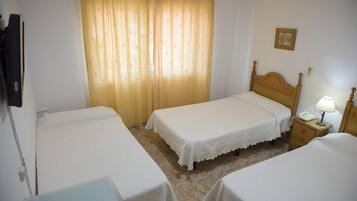 A hotel room with two single beds, a wooden nightstand with a lamp, a telephone, and a wall-mounted TV.