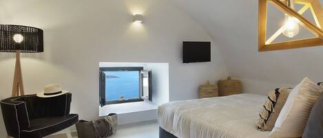 A bedroom with a large bed, a desk with a chair, a window with a view, and a hanging light fixture.