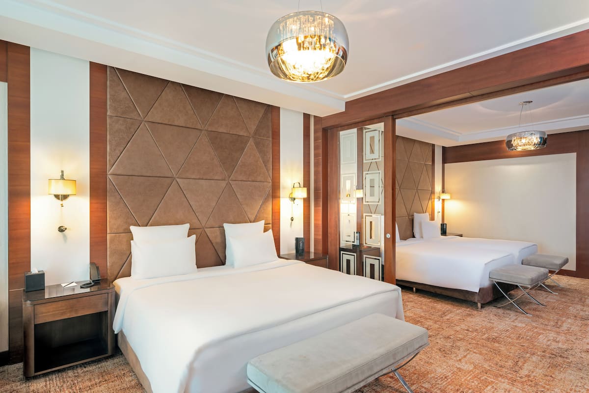 Ein Hotelzimmer mit einem großen Bett, einem kleineren Bett, einer Bank und einem Spiegel.