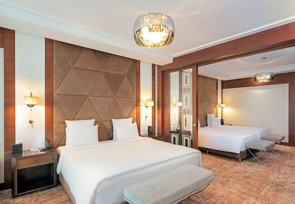 Una habitación de hotel con una cama grande, una cama más pequeña, un banco y un espejo.