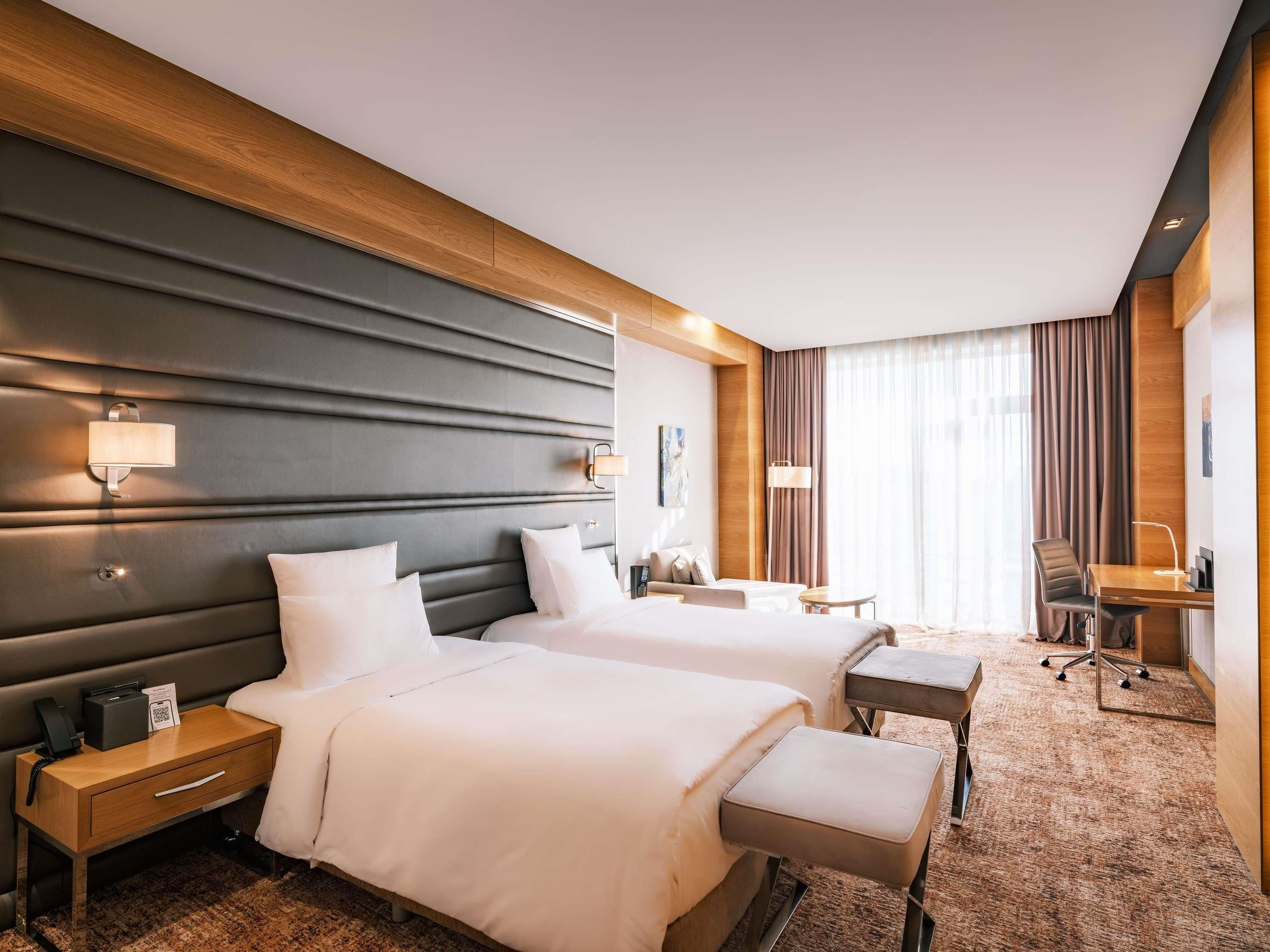 A hotel room with two beds, a desk, a chair, and a small table.