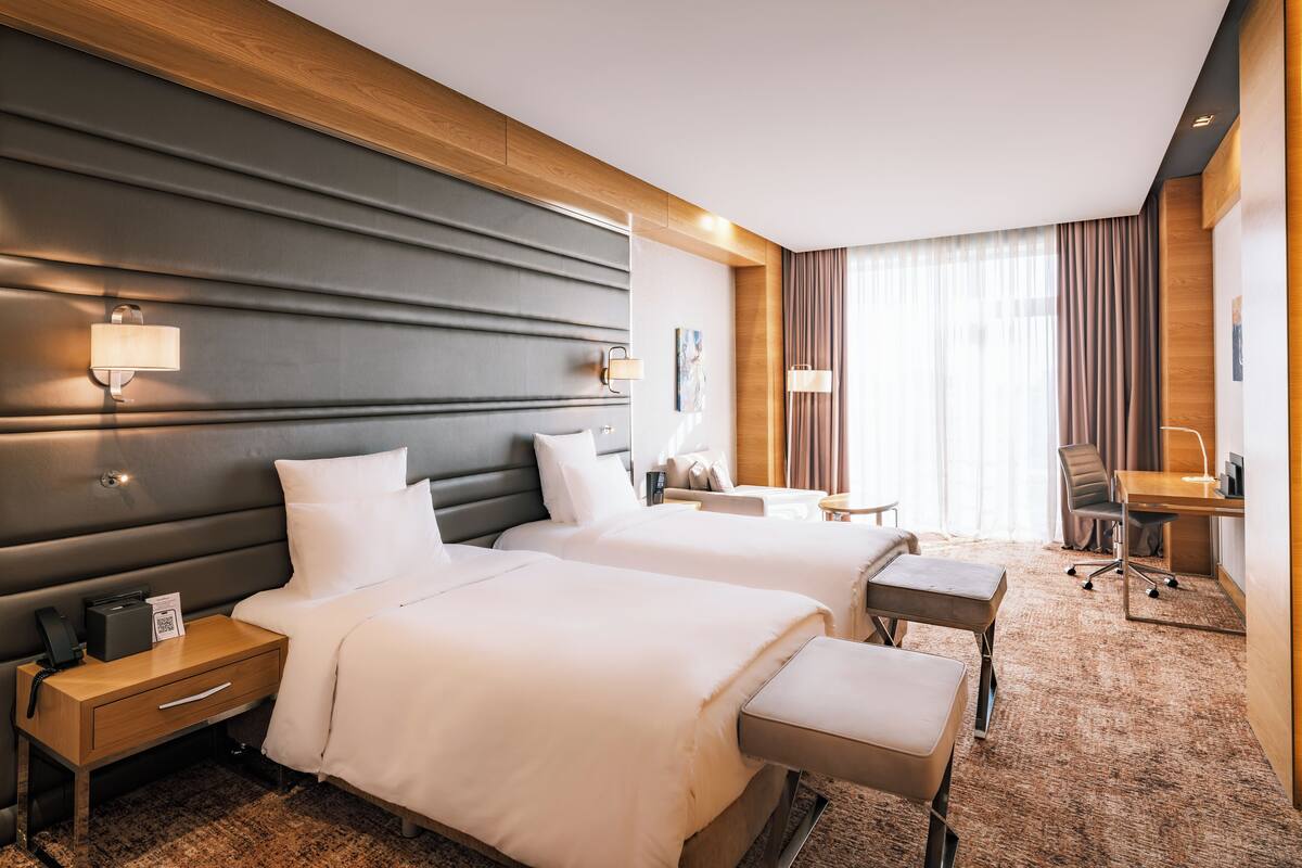 Ein Hotelzimmer mit zwei Betten, einem Schreibtisch, einem Stuhl, einem kleinen Tisch und einem Nachttisch.