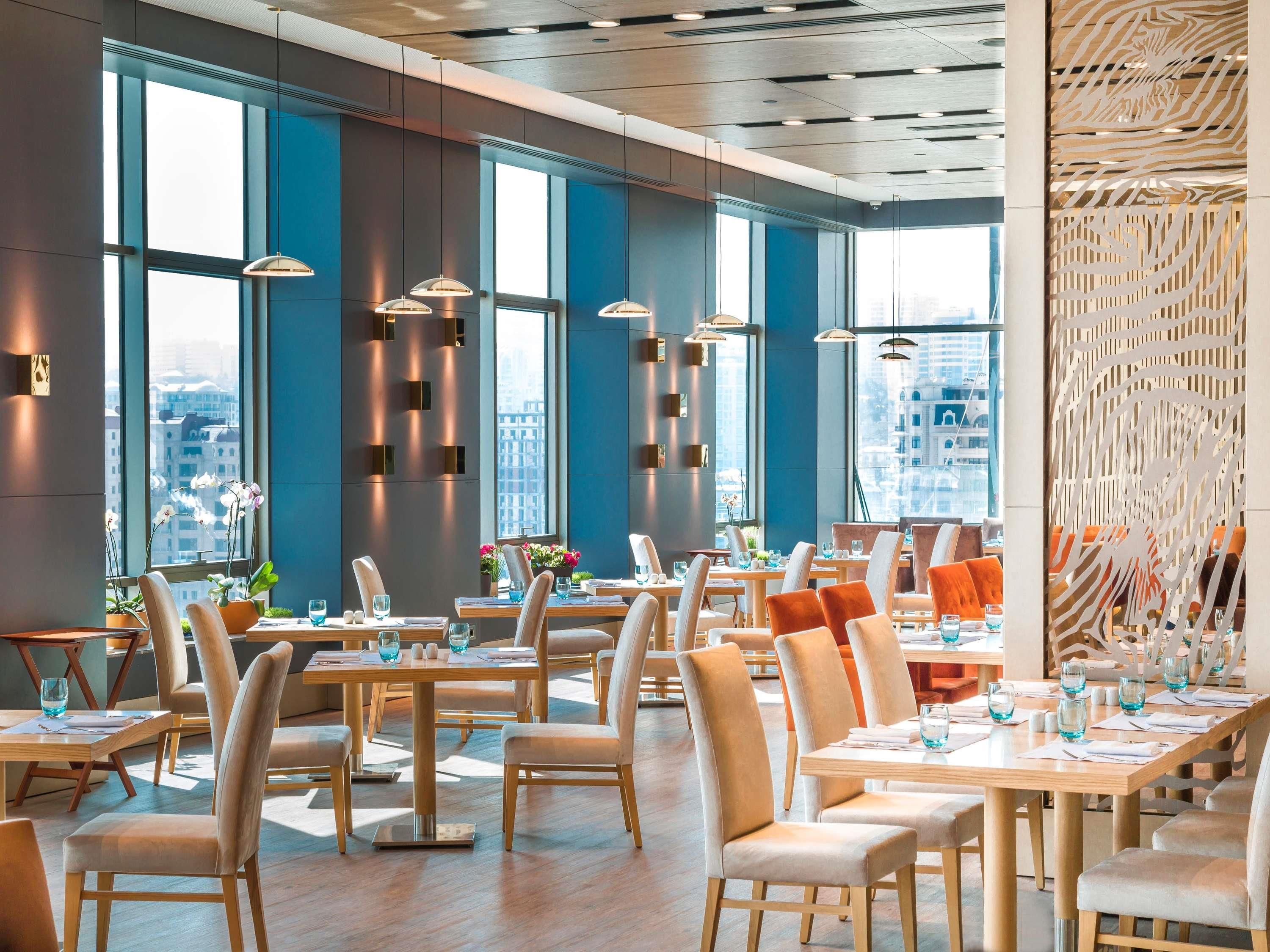 A modern dining area with tables and chairs, large windows, and pendant lighting.