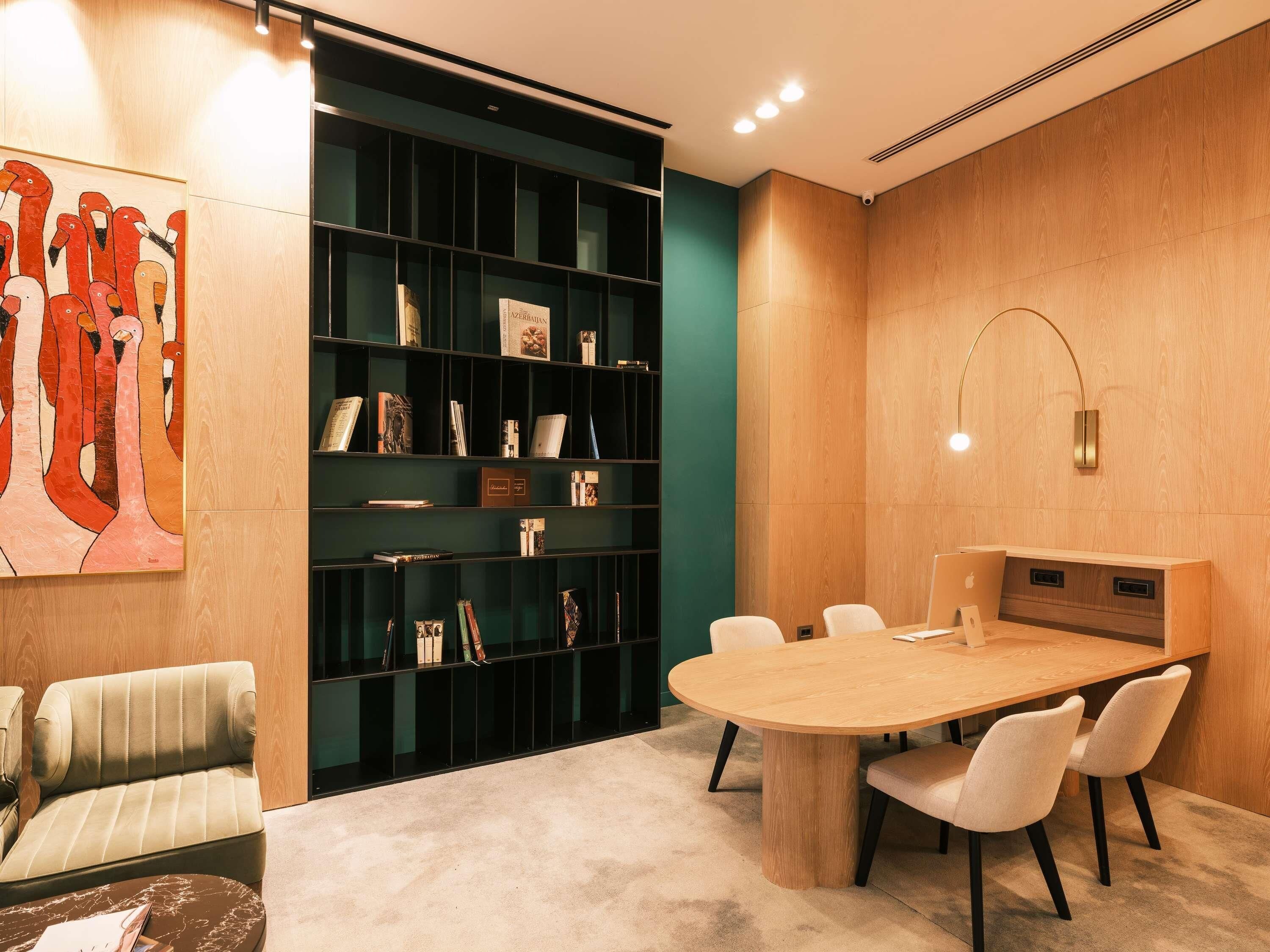 Uma sala de reunião moderna com uma mesa redonda, cadeiras, uma estante e um quadro na parede.