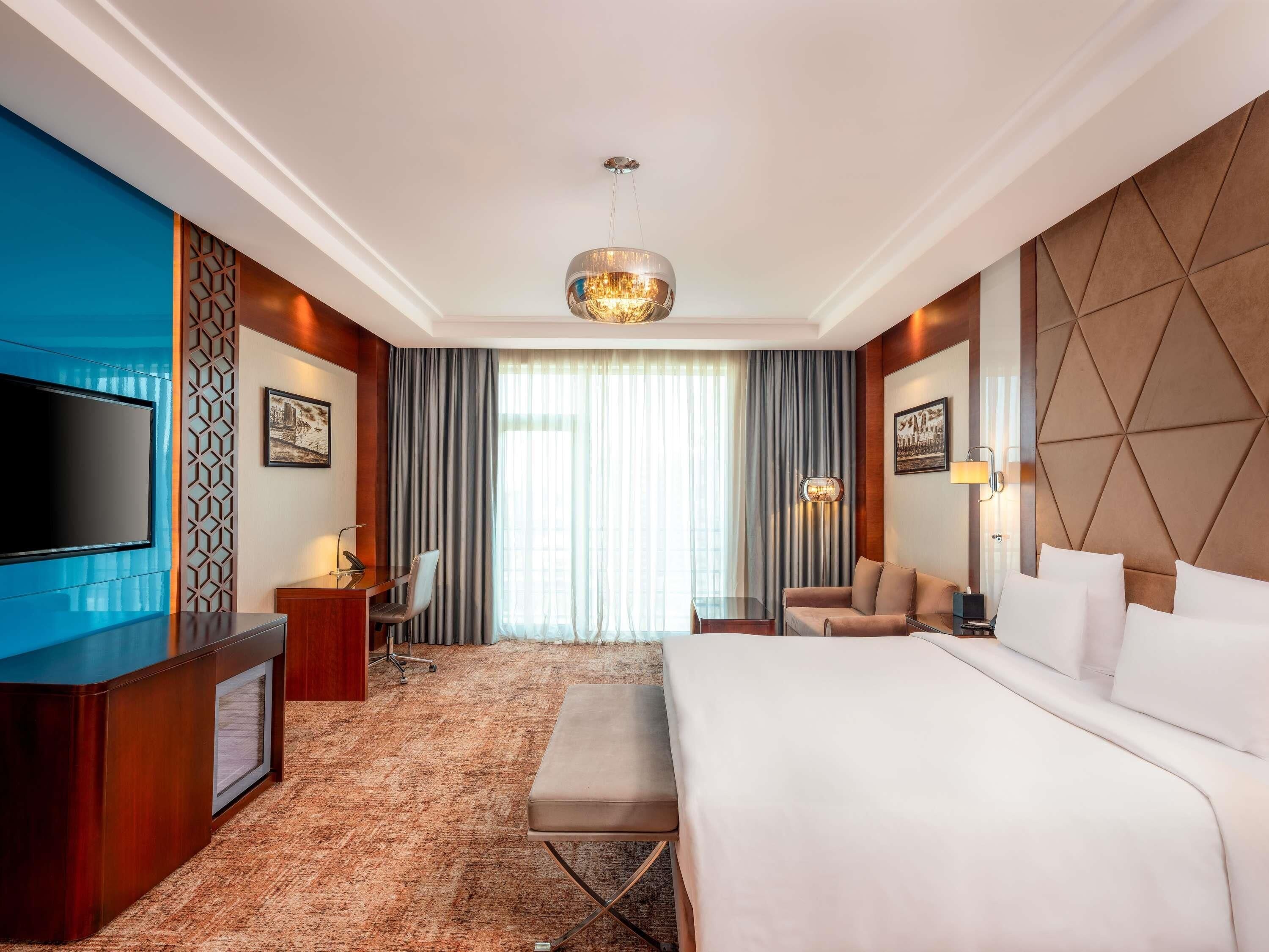 A hotel room with a large bed, a desk, a television, and a view of the outdoors through the window.