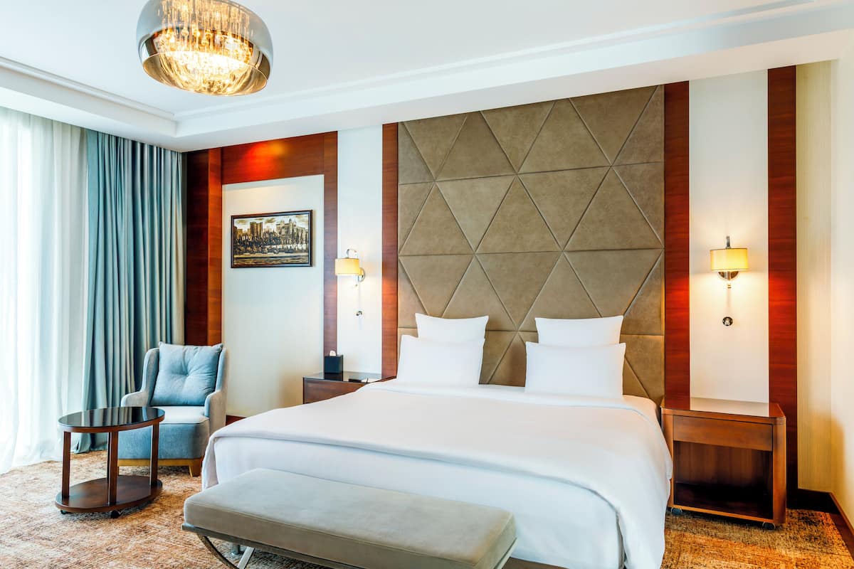 Ein Hotelzimmer mit einem großen Bett, einem Sessel, einem kleinen Tisch und einem Nachttisch.