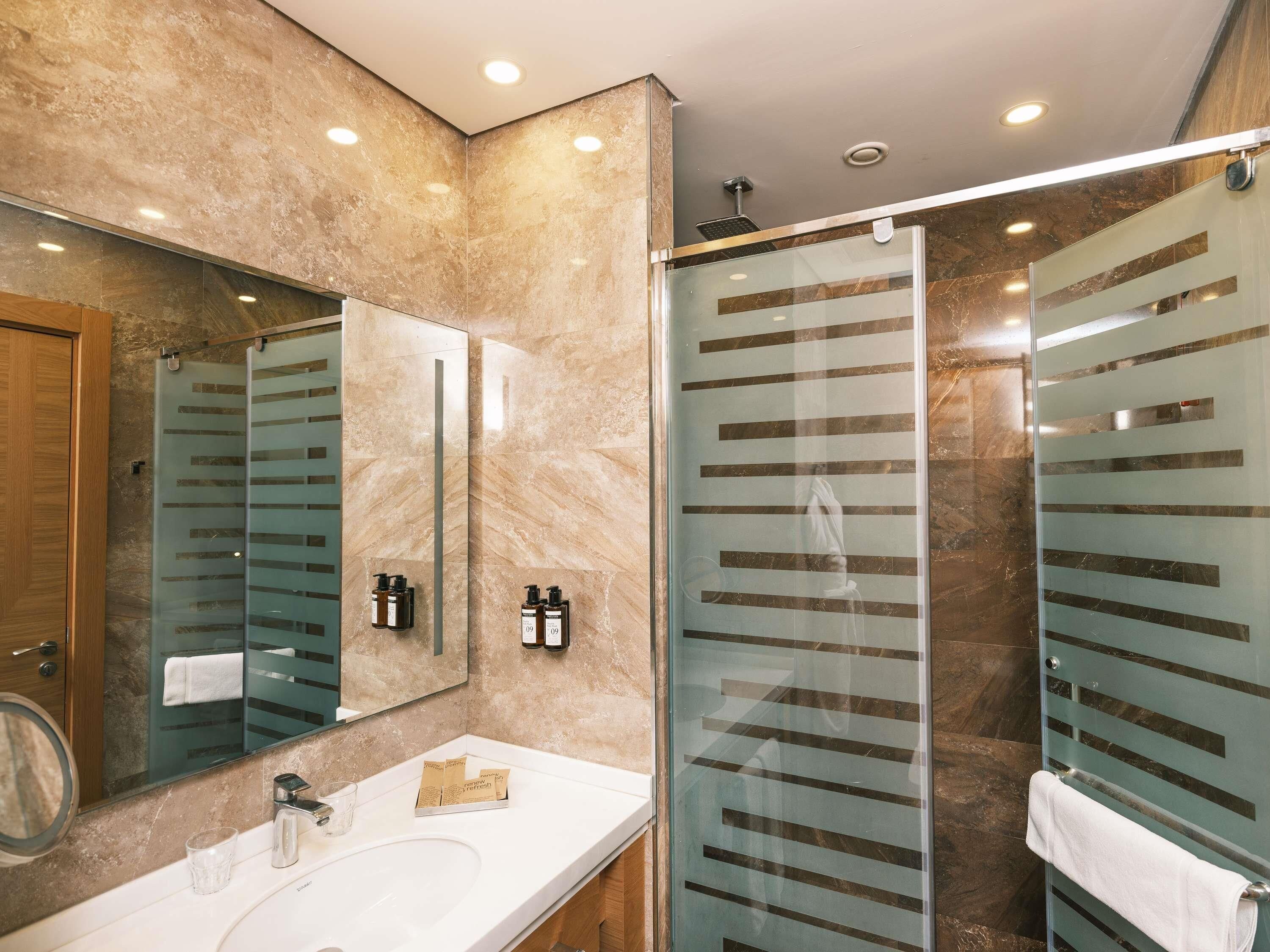 A modern bathroom with a glass shower enclosure, a large mirror, and a white sink.
