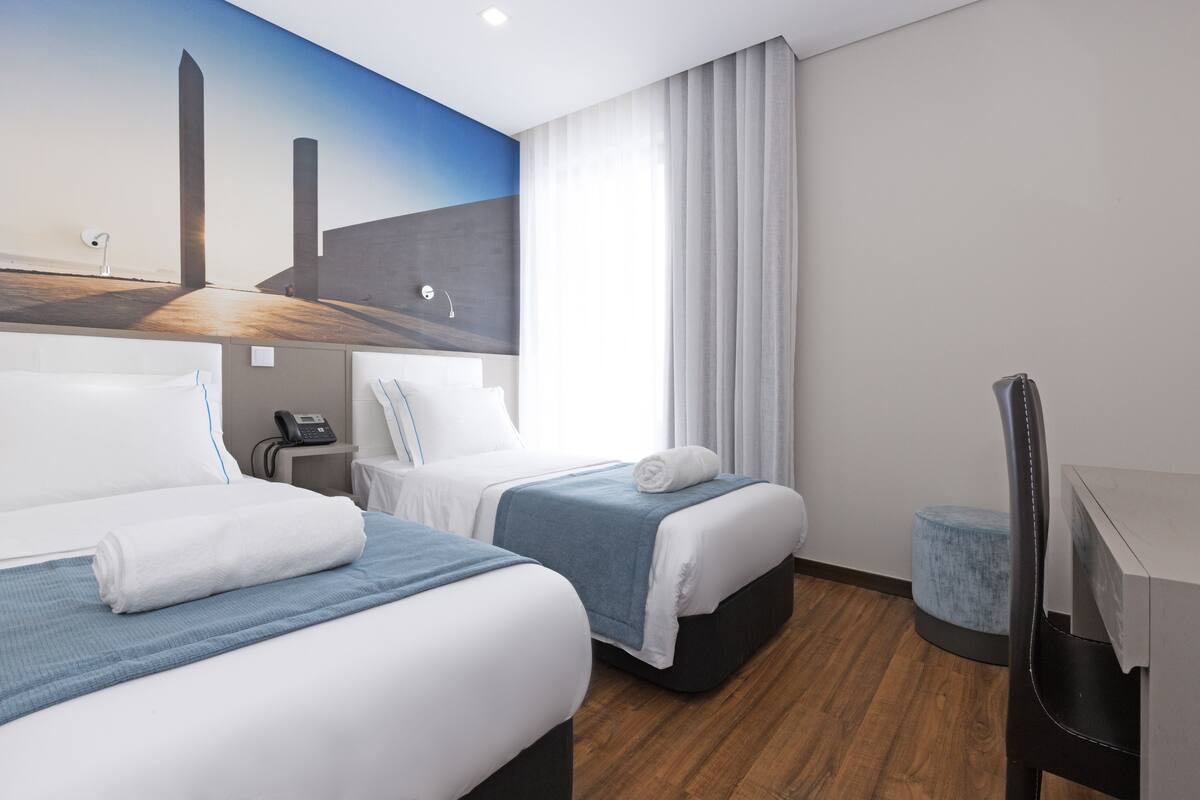 Une chambre d’hôtel avec deux lits, un bureau, une chaise et une grande fresque murale.