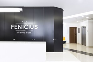 Un'accogliente area reception di un hotel moderno, con un elegante bancone nero e un cartello che recita "FENICIUS charme hotel".