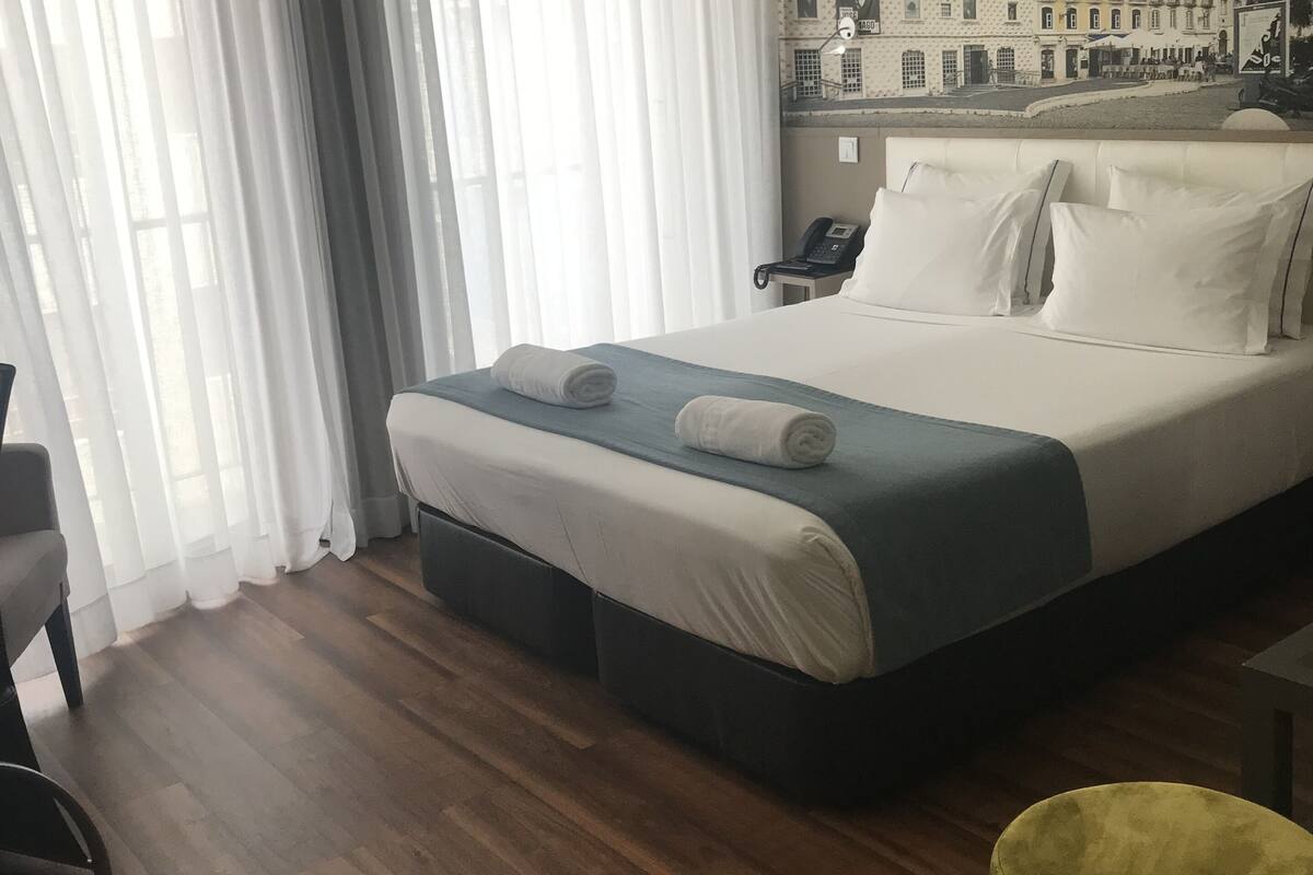 A hotel room with a large bed, a desk, a chair, and a yellow ottoman.