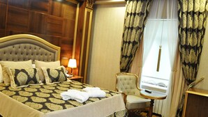 A hotel room with a large bed, a sitting area with a chair and a small table, a lamp, and a window with curtains. - Joyy Hotel & Spa (Baku)