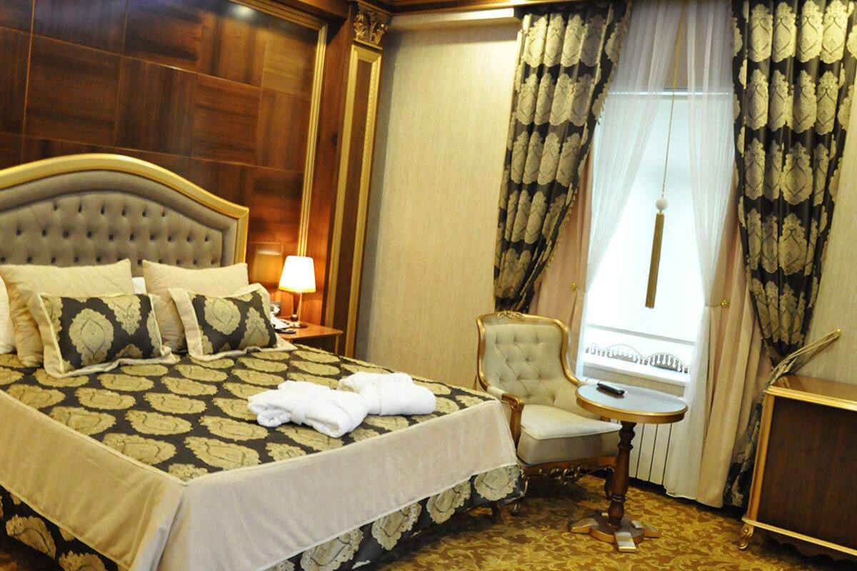 A hotel room with a large bed, a sitting area with a chair and a small table, a lamp, and a window with curtains.