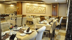 A dining area with multiple tables set for meals, featuring beige chairs and a checkered floor. - Joyy Hotel & Spa (Baku)