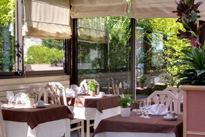Un espace de restauration en plein air avec des tables pour deux, protégées par des auvents et agrémentées de plantes en pot.