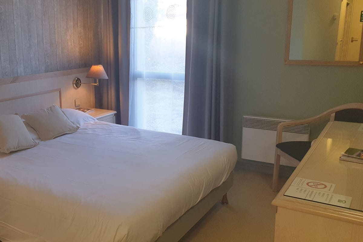 Habitació d'hotel amb un llit gran, dues làmpades de nit, un escriptori amb una cadira i una finestra amb cortines.