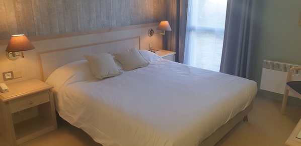 Una cama bien hecha con sábanas blancas, dos lámparas de noche, una mesita de noche con un teléfono y una silla.