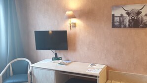 Habitació d'hotel amb televisió de pantalla plana, escriptori amb làmpada, cadira, llit i un quadre de toros a la paret.