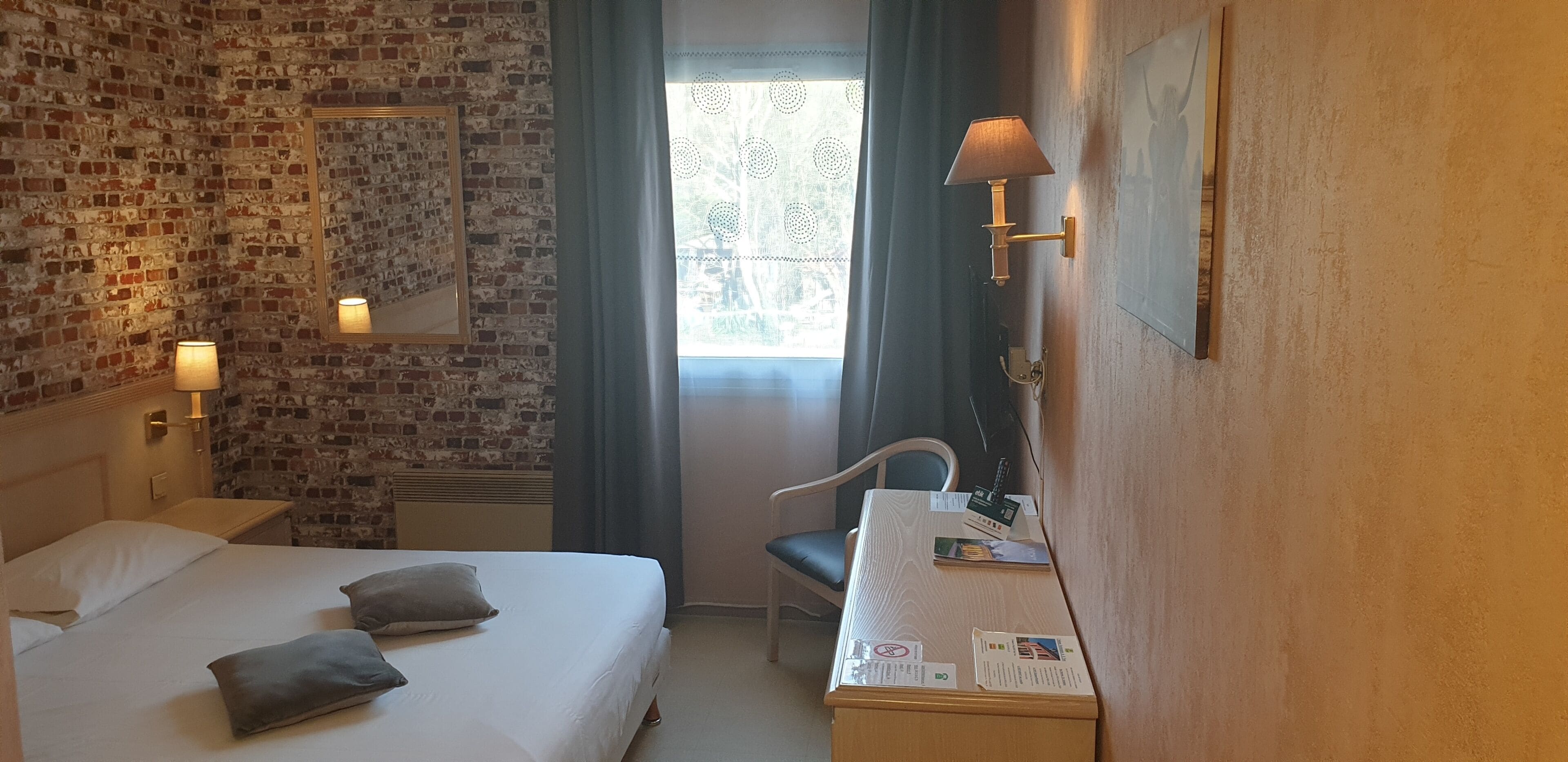 Habitación de hotel con pared de ladrillo, cama con almohadas, escritorio con lámpara y una silla.