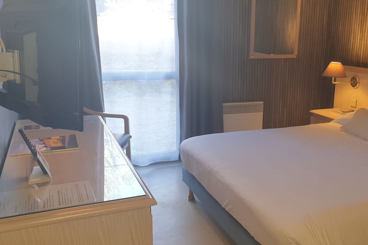 Ein Hotelzimmer mit einem Bett, einem Schreibtisch mit Stuhl, einer Lampe und einem Fenster mit Vorhängen.