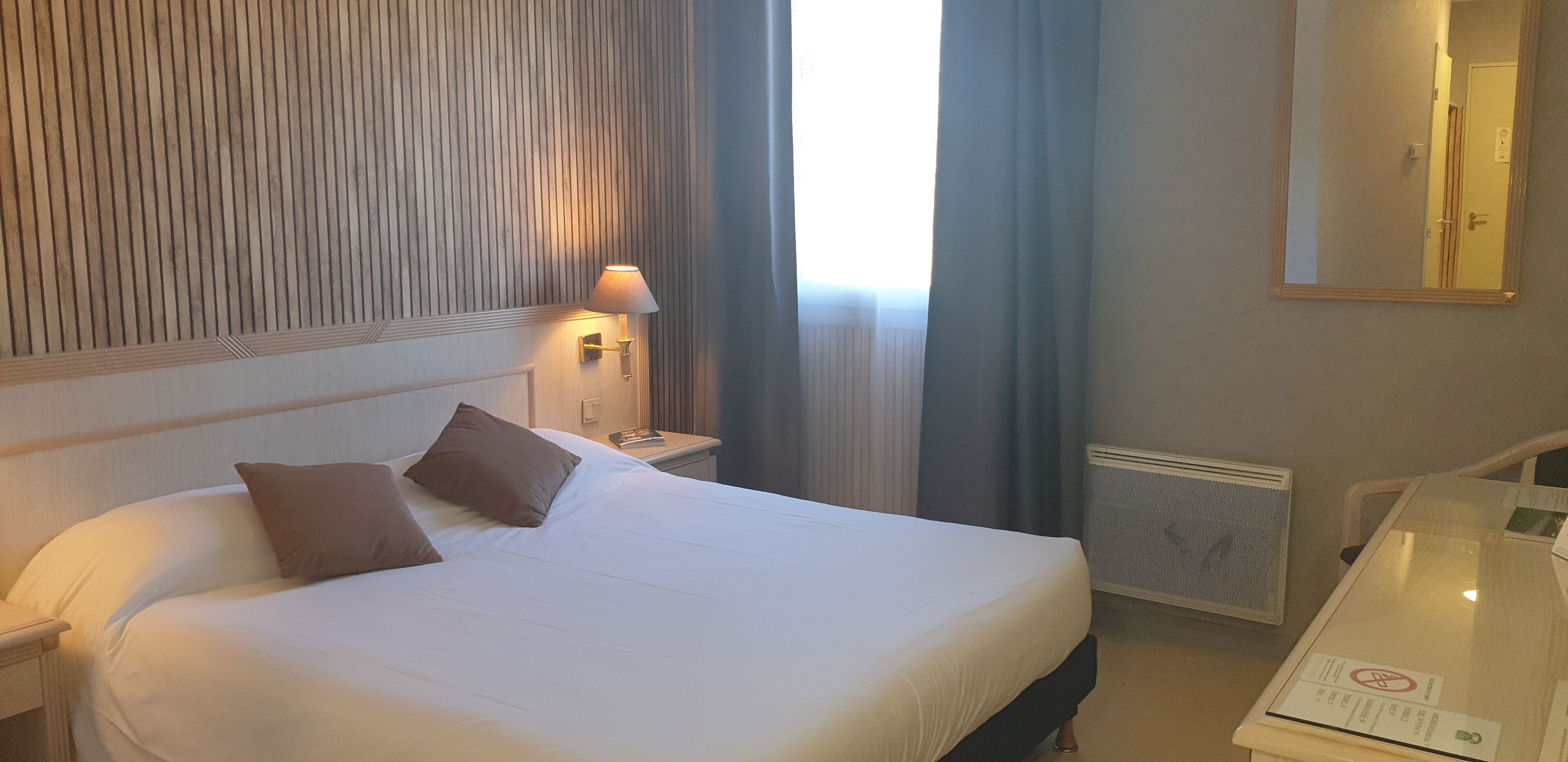 Ein Hotelzimmer mit Bett, Nachttisch, Lampe, Spiegel und einem Tisch mit einem Schild.
