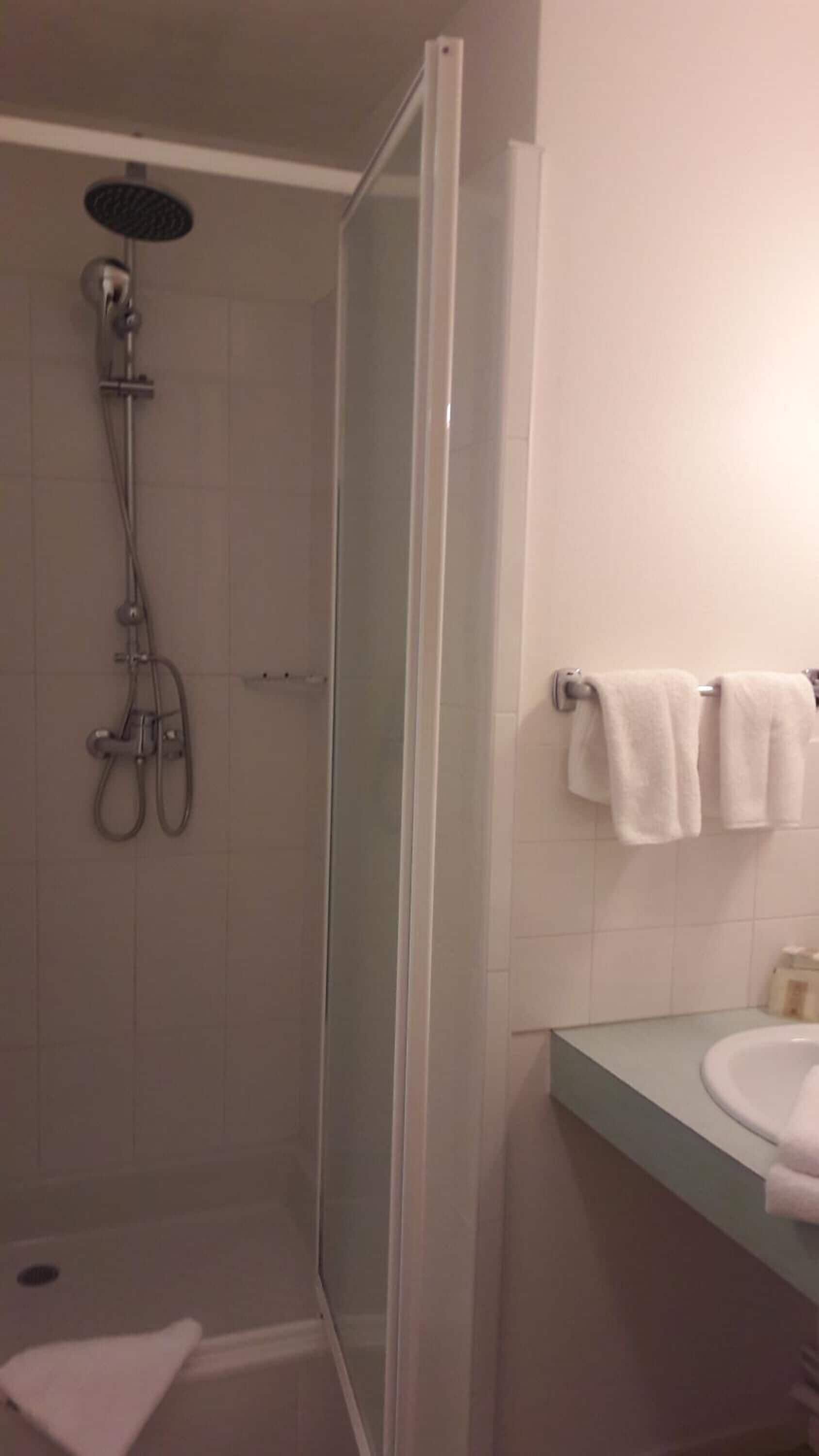 Ducha con puerta de cristal, lavabo con espejo y dos toallas en un perchero.