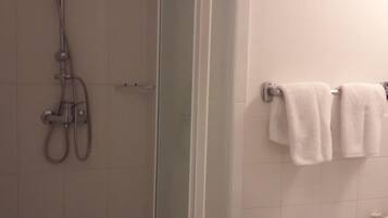 Ducha con puerta de cristal, lavabo con espejo y dos toallas en un perchero.